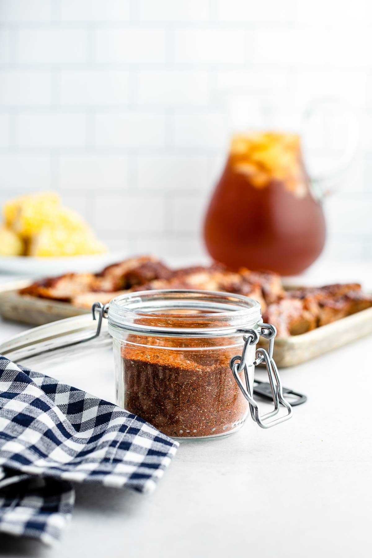 dry rub in jar with ribs with ribs and iced tea pitcher in background
