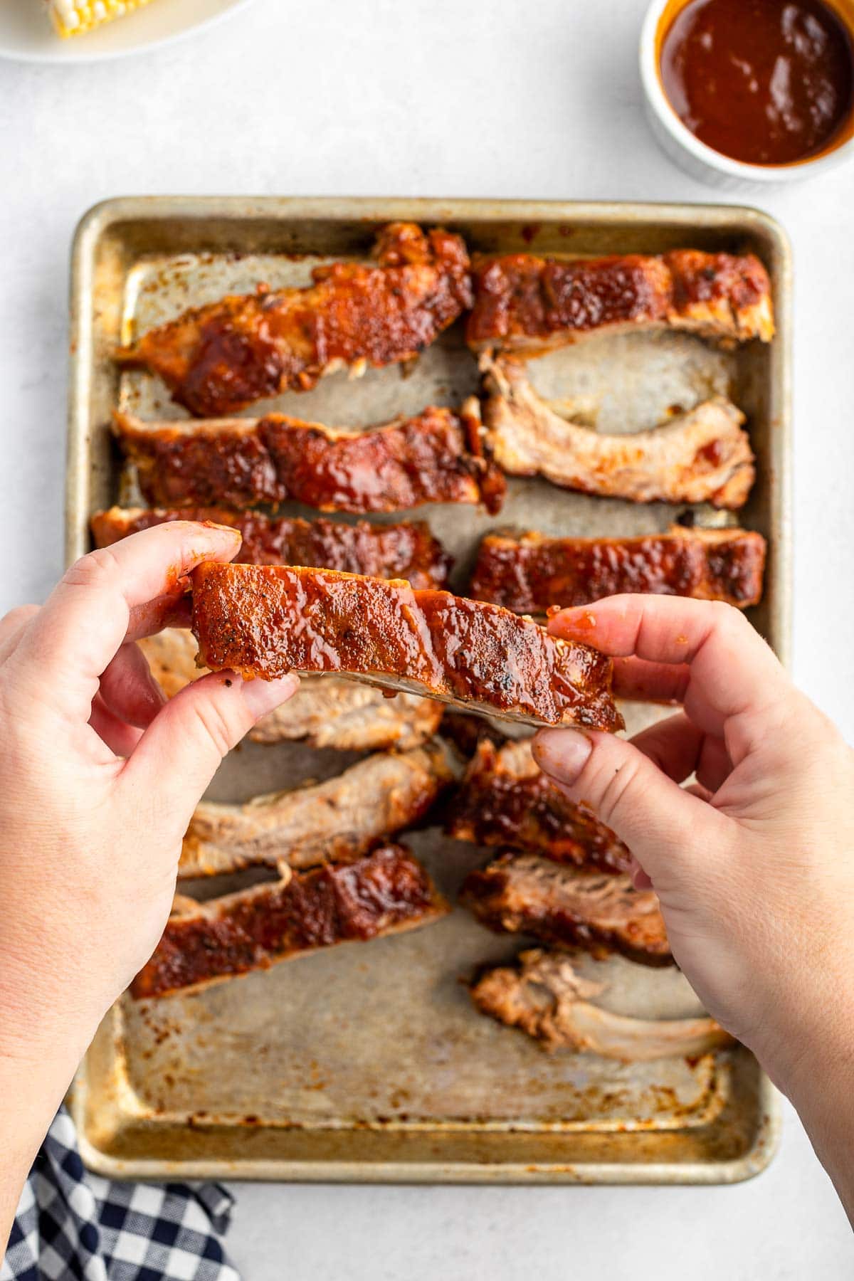 hands holding a baked baby back rib with BBQ sauce