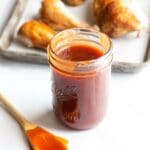 pint Mason jar of homemade barbecue sauce with chicken on sheet pan in background