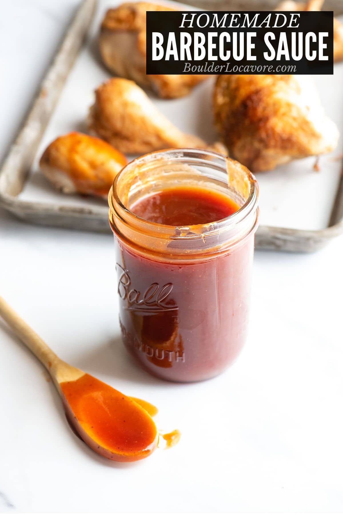 pint Mason jar of homemade barbecue sauce with chicken on sheet pan in background