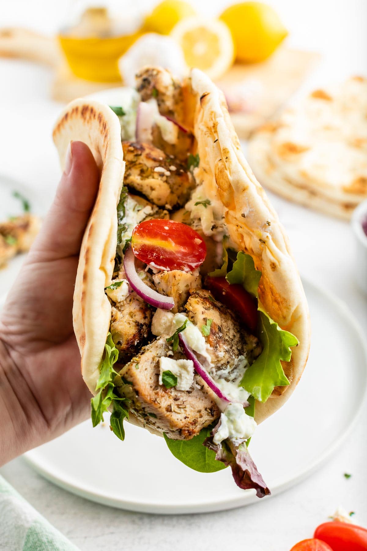 hand holding a soft flatbread folded with chicken souvlaki, tomatoes, onions and feta cheese inside