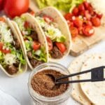 homemade taco seasoning in a small jar with tacos behind
