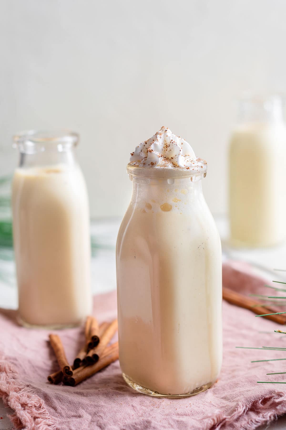 A glass of eggnog topped with whipped cream and a cinnamon stick