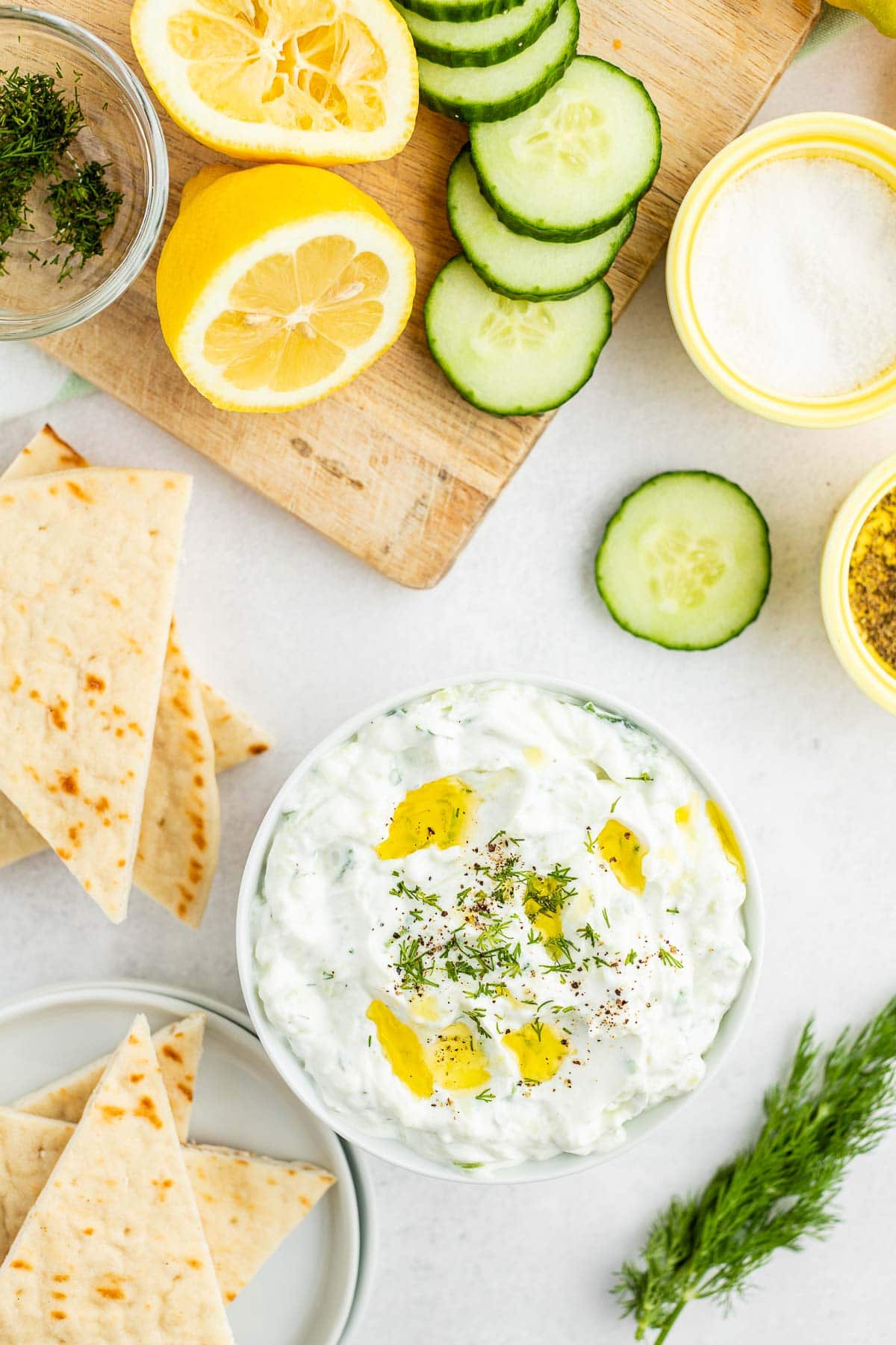 bowl of tzatziki sauce with pita triangles and slices of cucumber and lemons from overhead