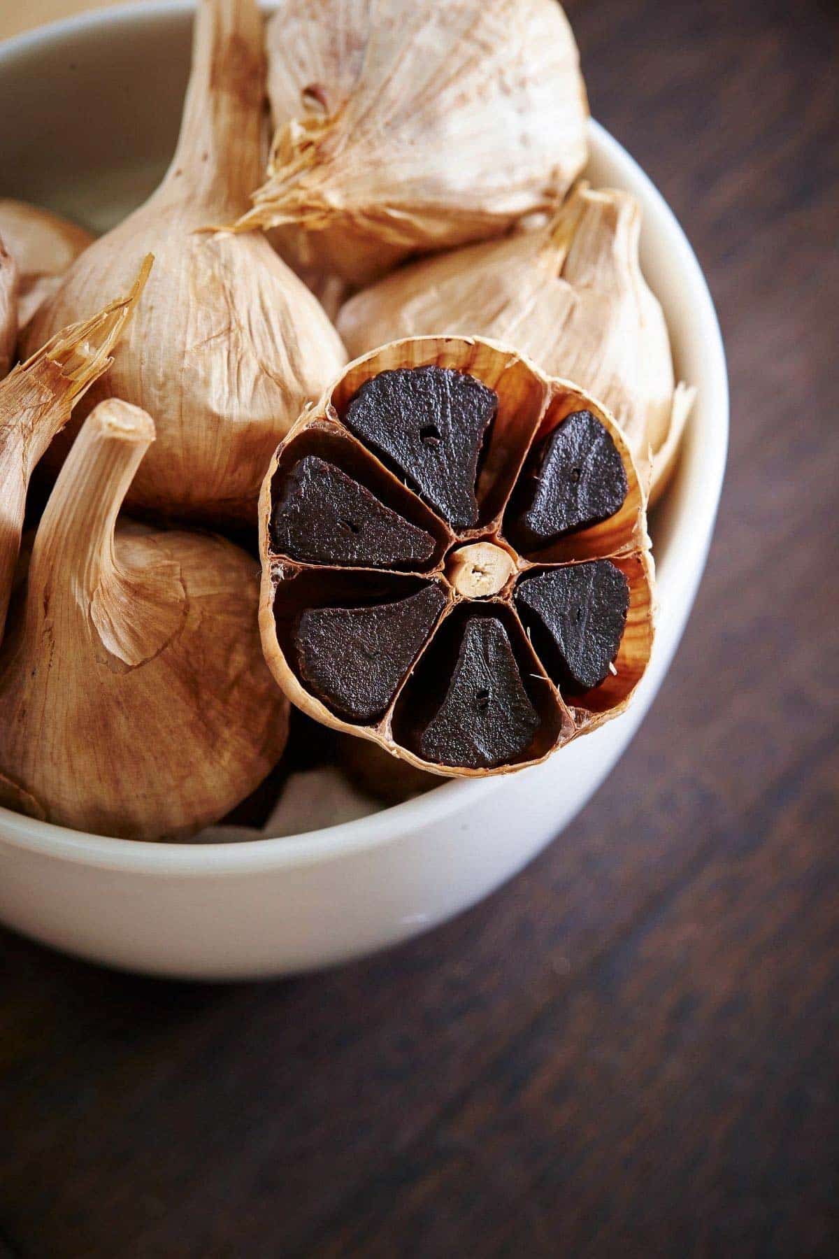 close up black garlic cloves in white bowl