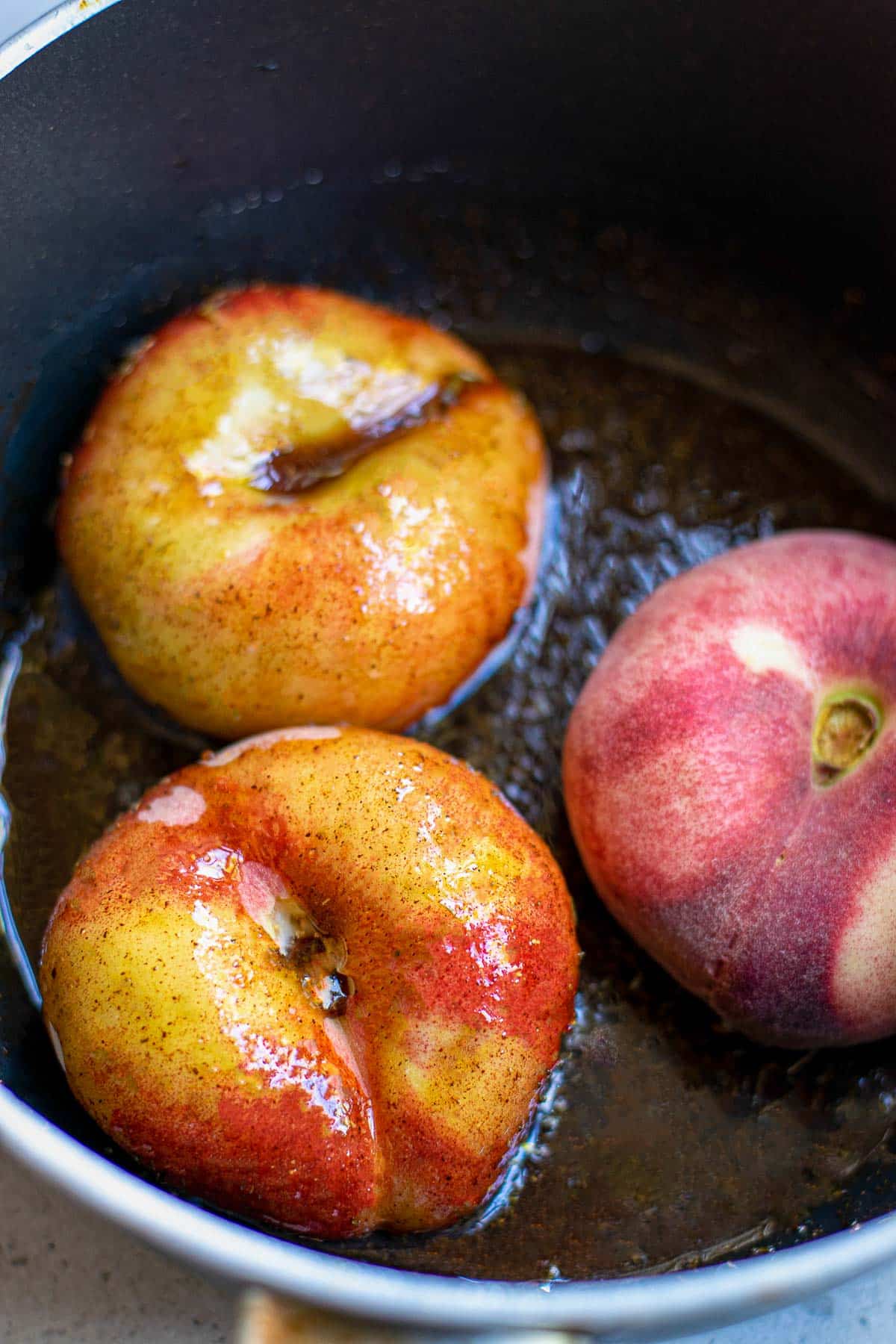 donut peaches in saucepan with sauce