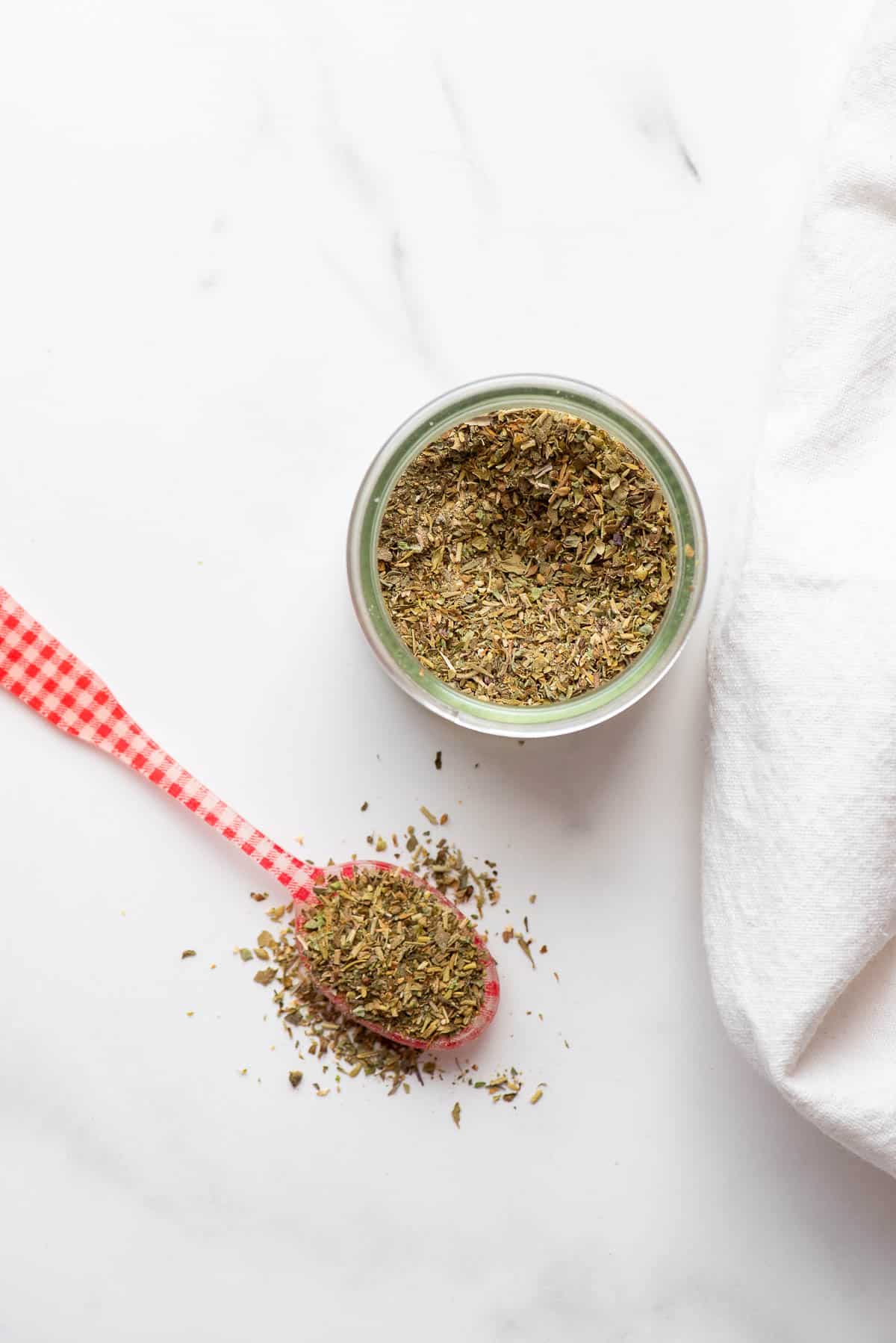 Italian seasoning in jar and on spoon from overhead