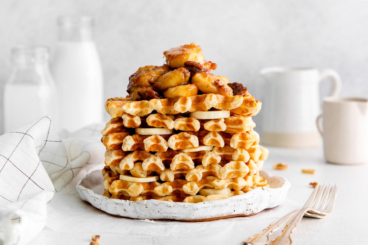 stack o homemade waffles with bananas foster topping side view.