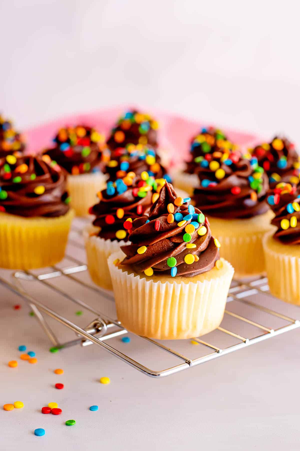yellow cupcakes with chocolate frosting and sprinkles on rack.