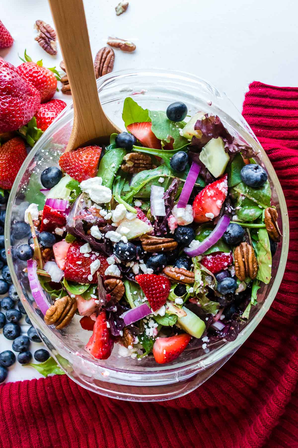 tossed strawberry salad with blueberries, goat cheese, red onions in a clear glass bowl